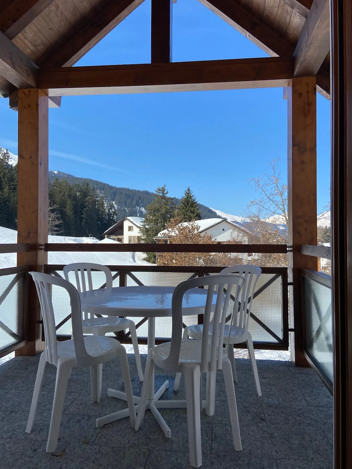 Überdachte Terrasse mit Tisch und Stühlen, dahinter verschneite Wälder und Berge